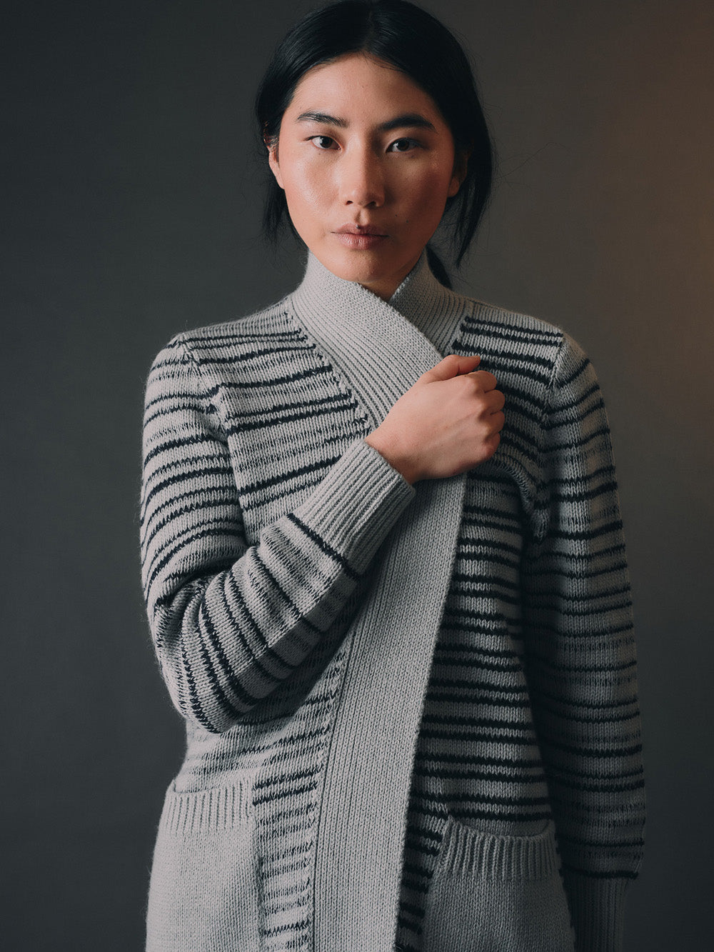 Woman wearing a long, stripe-patterned cardigan against a dark background