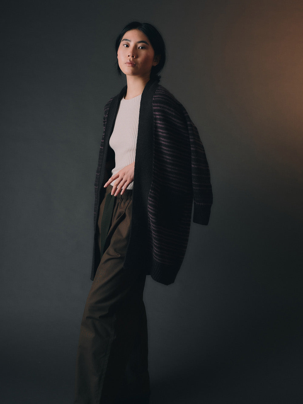 Woman wearing a long, dark stripe-patterned cardigan against a dark background