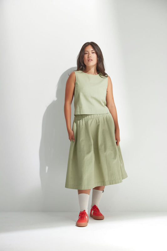 Woman wearing a light green sleeveless top and skirt with red shoes on a white background