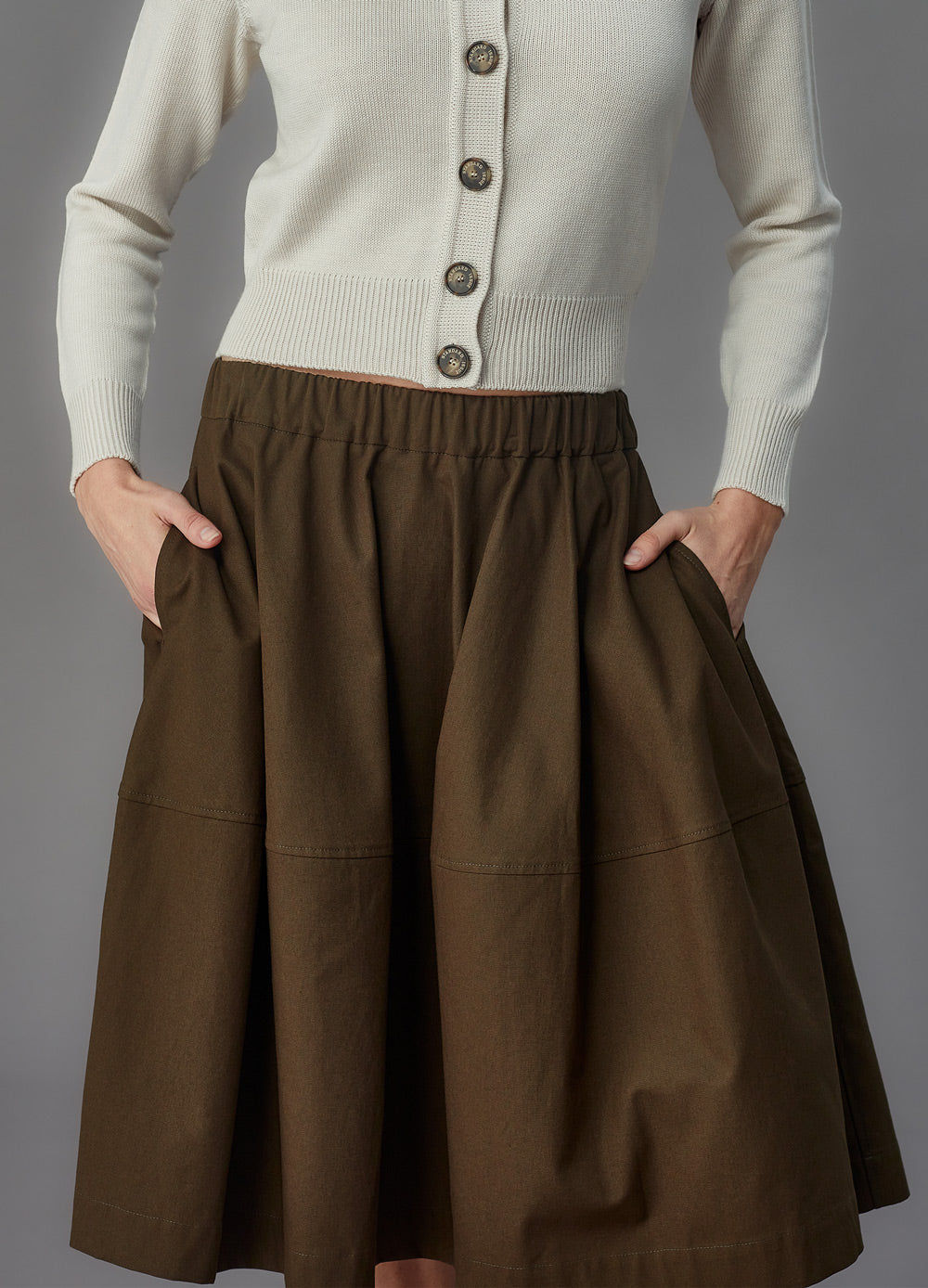 Woman wearing an alabaster cardigan and green skirt on a gray background