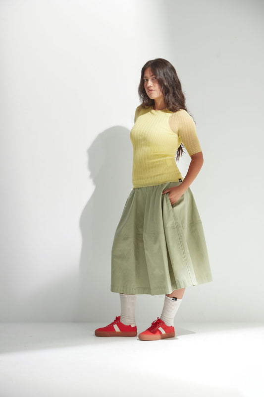 Woman wearing a yellow top and light green skirt with red shoes on a white background.