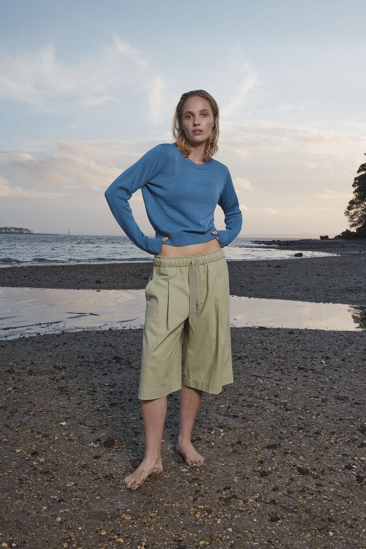 Woman standing on a beach wearing a blue sweater and light green shorts.