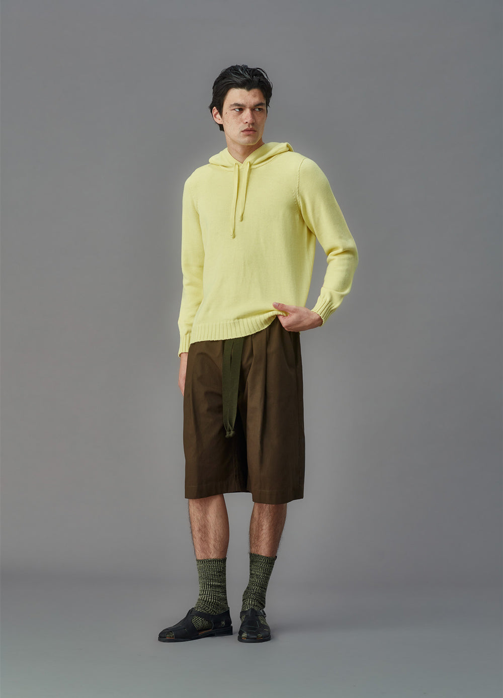 Person wearing a light yellow hoodie and green shorts on a gray background