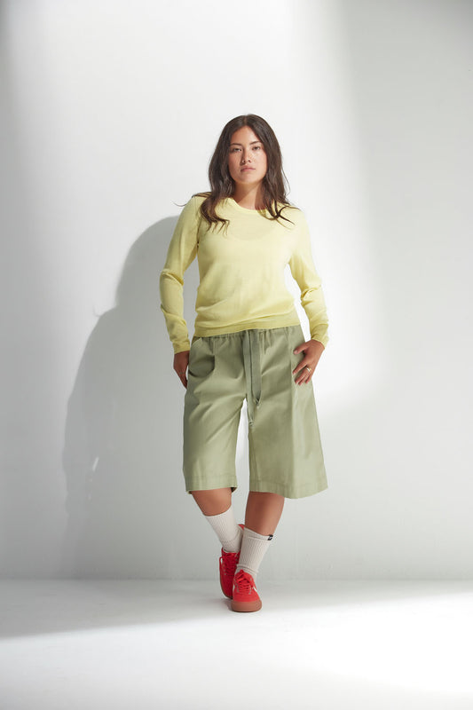Woman wearing a yellow sweater and light green pants against a white background