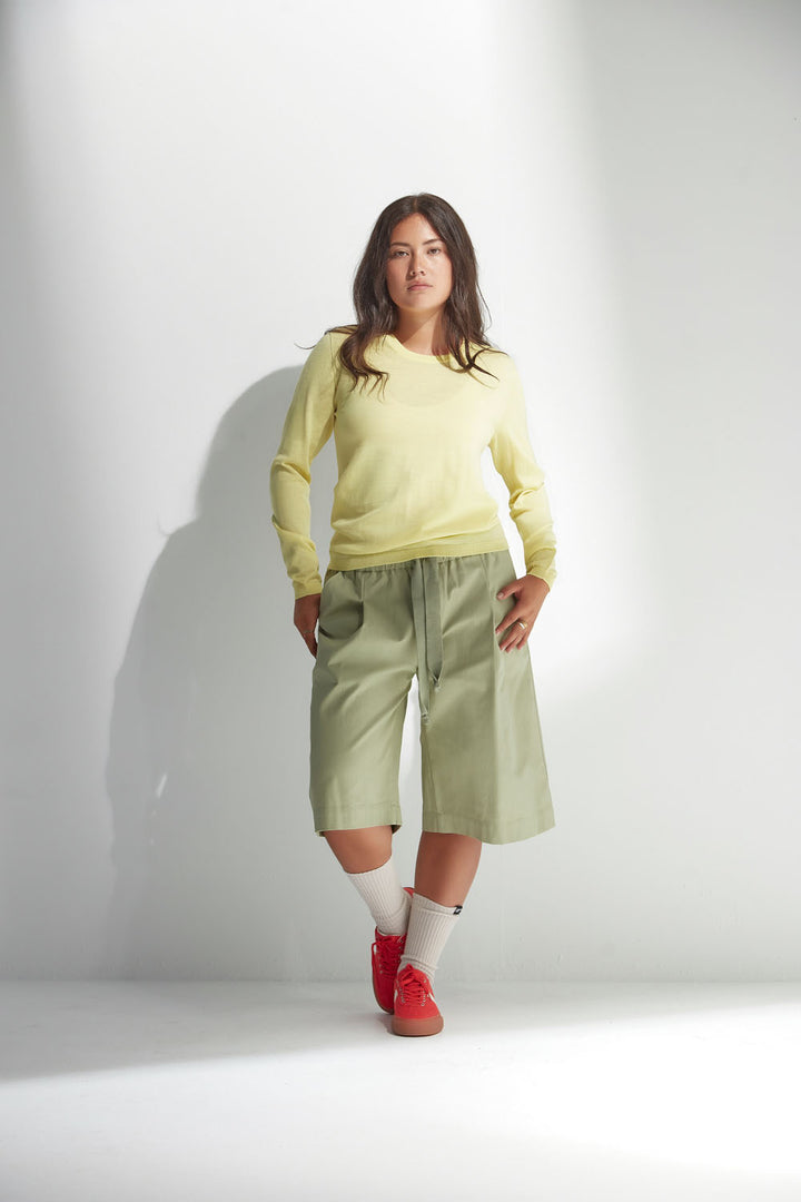 Woman wearing a yellow sweater and light green pants against a white background