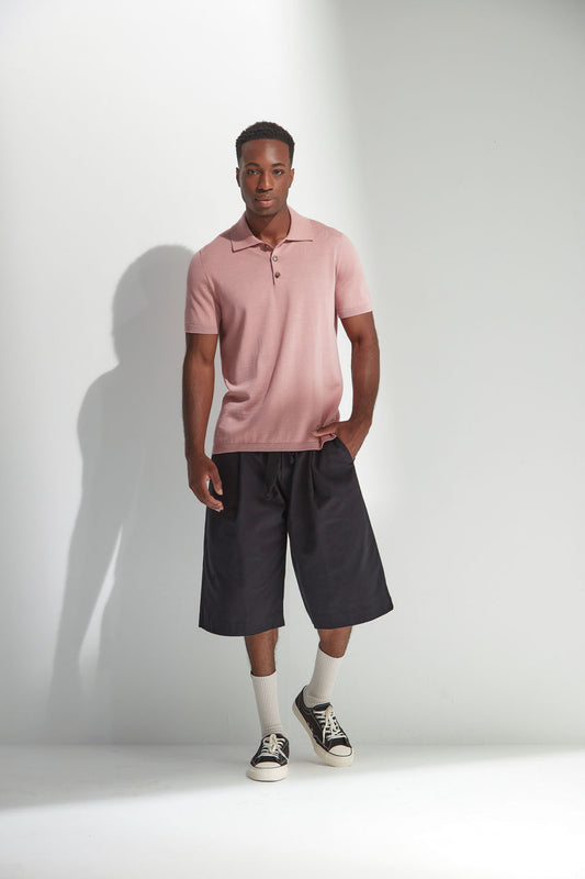 Man wearing a pink polo shirt and black shorts standing against a white background