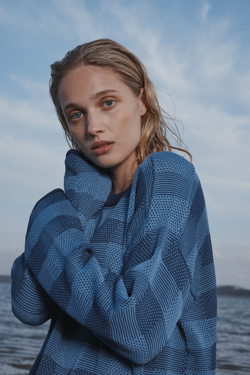 Woman wearing a blue and white checkered knitted sweater with a blue sky background