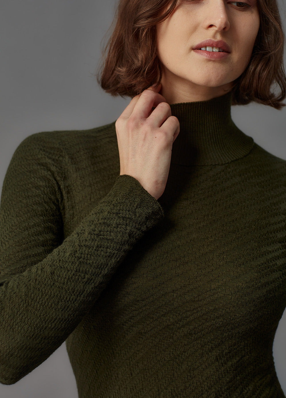 Woman wearing a dark green turtleneck dress against a neutral background