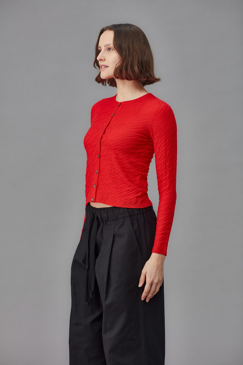 Woman wearing a red cardigan and black pants against a gray background
