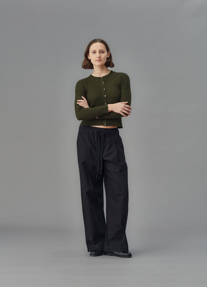 Person wearing a green cardigan and black pants on a gray background