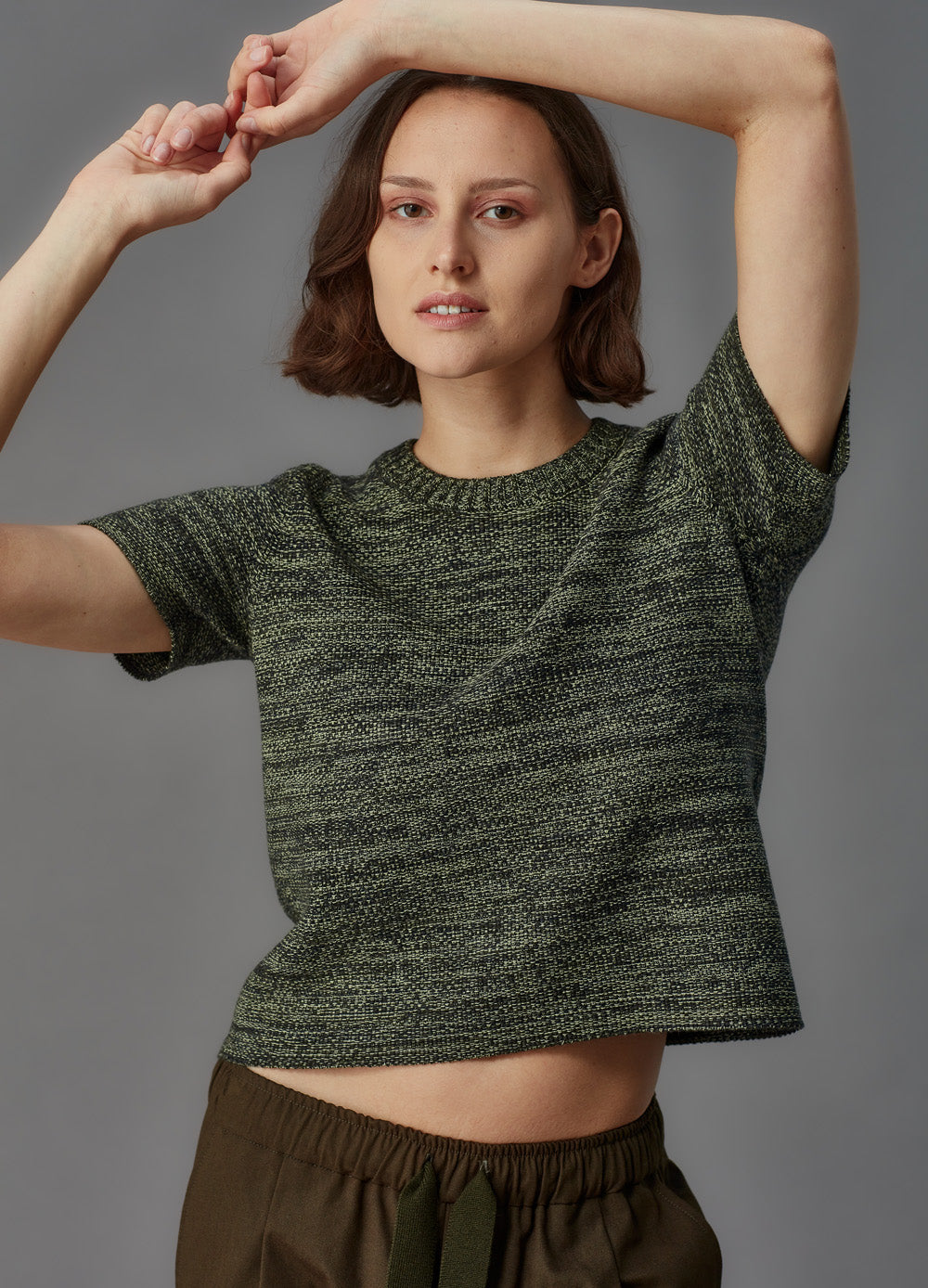 Woman wearing a green knitted top against a gray background