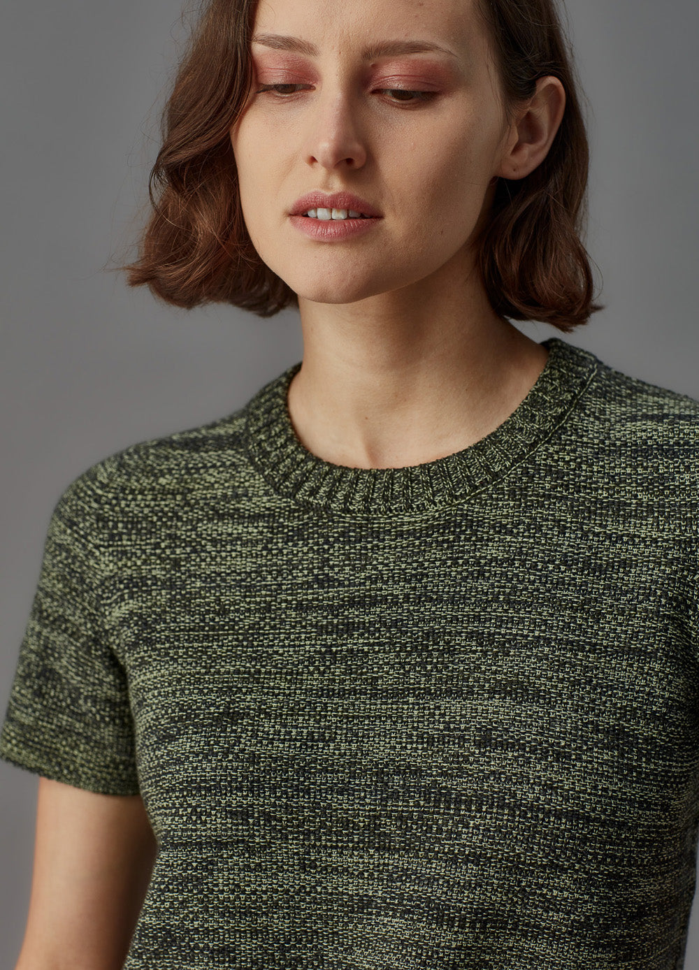 Woman wearing a green knitted sweater against a gray background