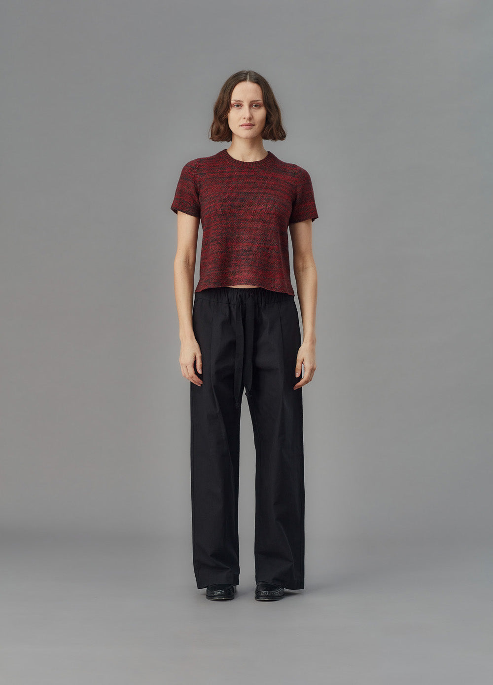 Person wearing a red patterned shirt and black pants on a gray background