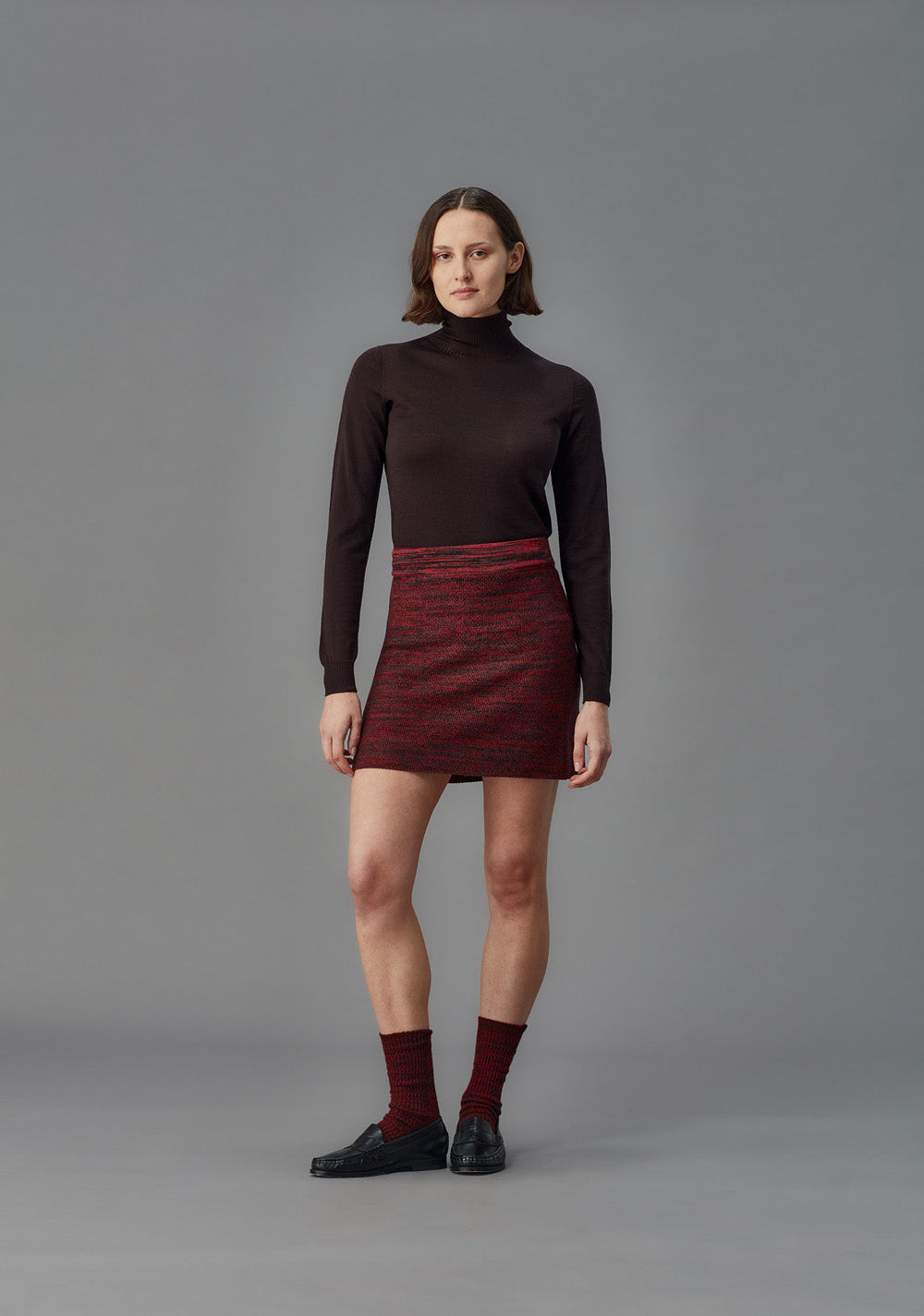 Woman wearing a red knit skirt and brown turtleneck on a gray background
