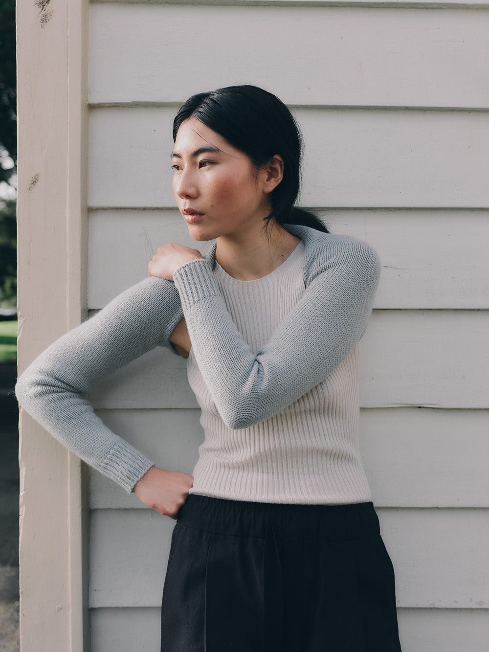 Woman wearing a light blue bolero sleeves over a beige top, standing against a light-colored wall.