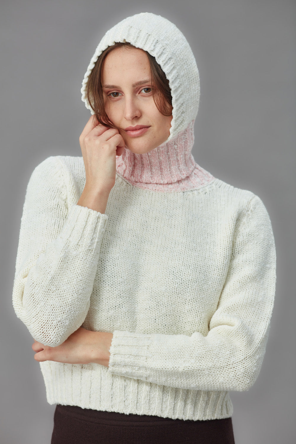 Woman wearing a white knitted boucle balaclava and sweater against a gray background