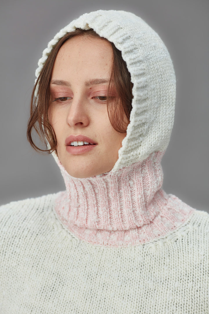 Person wearing a white knitted boucle balaclava against a gray background