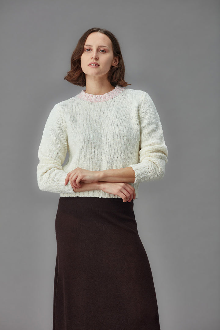 Woman wearing a white textured boucle sweater and dark skirt against a gray background