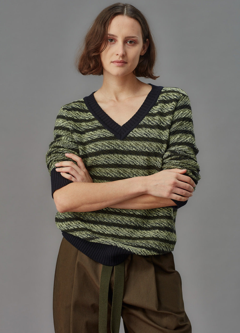 Person wearing a green and black striped sweater with brown pants on a gray background