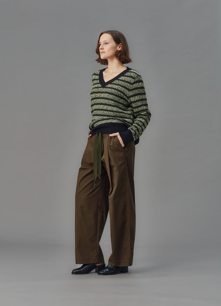 Woman wearing a green and black striped sweater with brown pants on a gray background