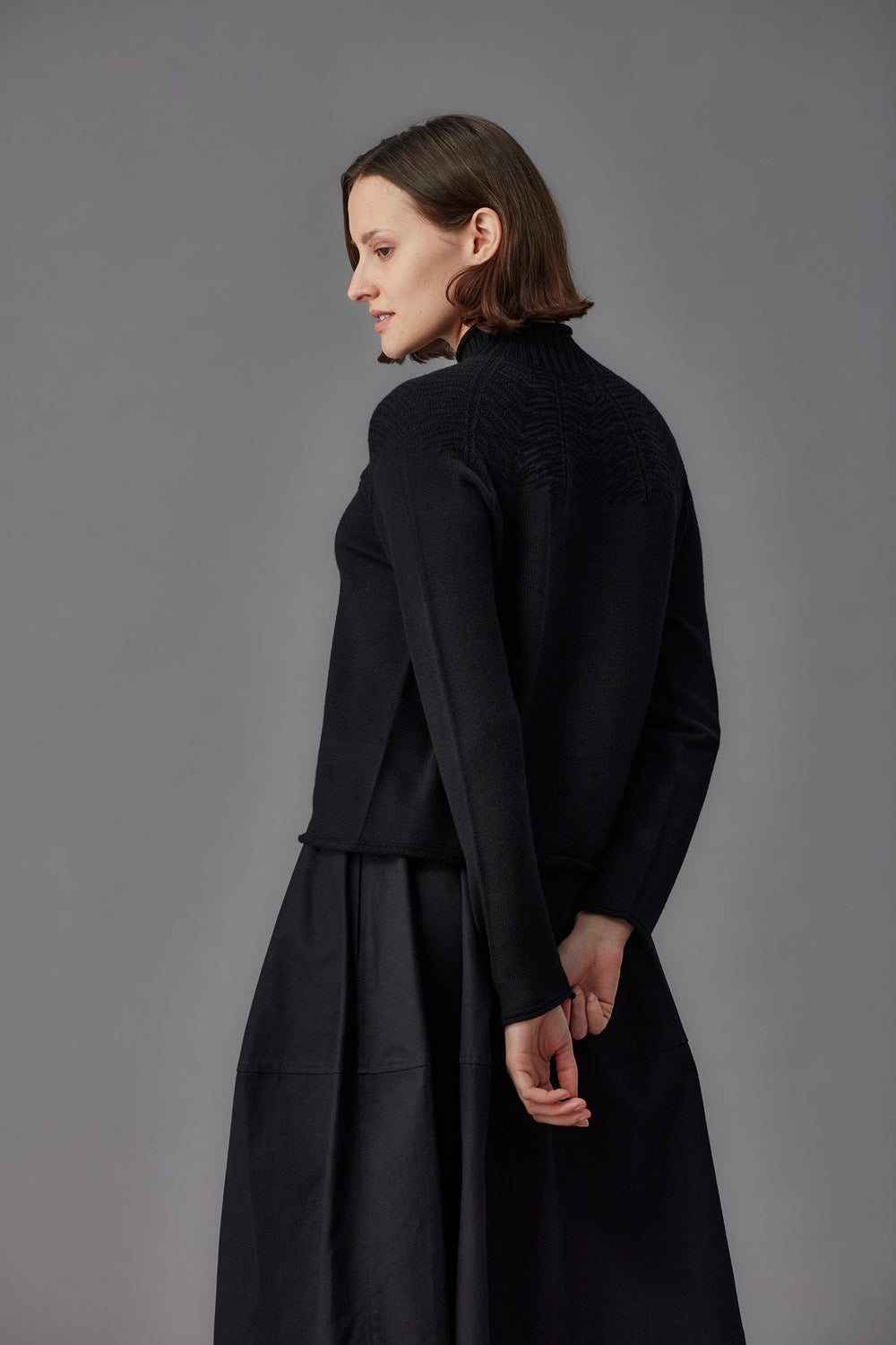 Woman wearing a black mock neck sweater and black skirt against a gray background