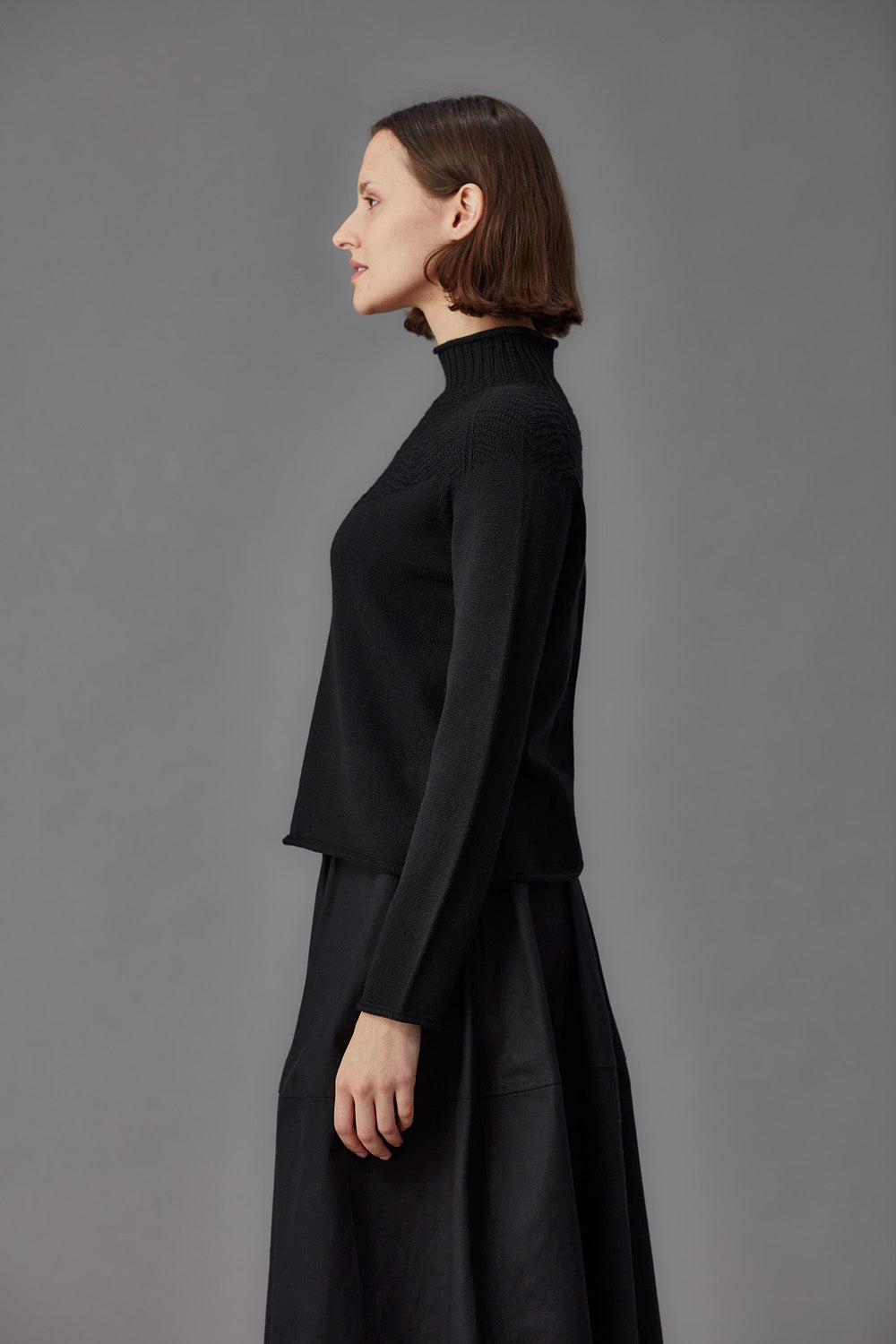 Woman wearing a green mock neck sweater and black skirt against a gray background