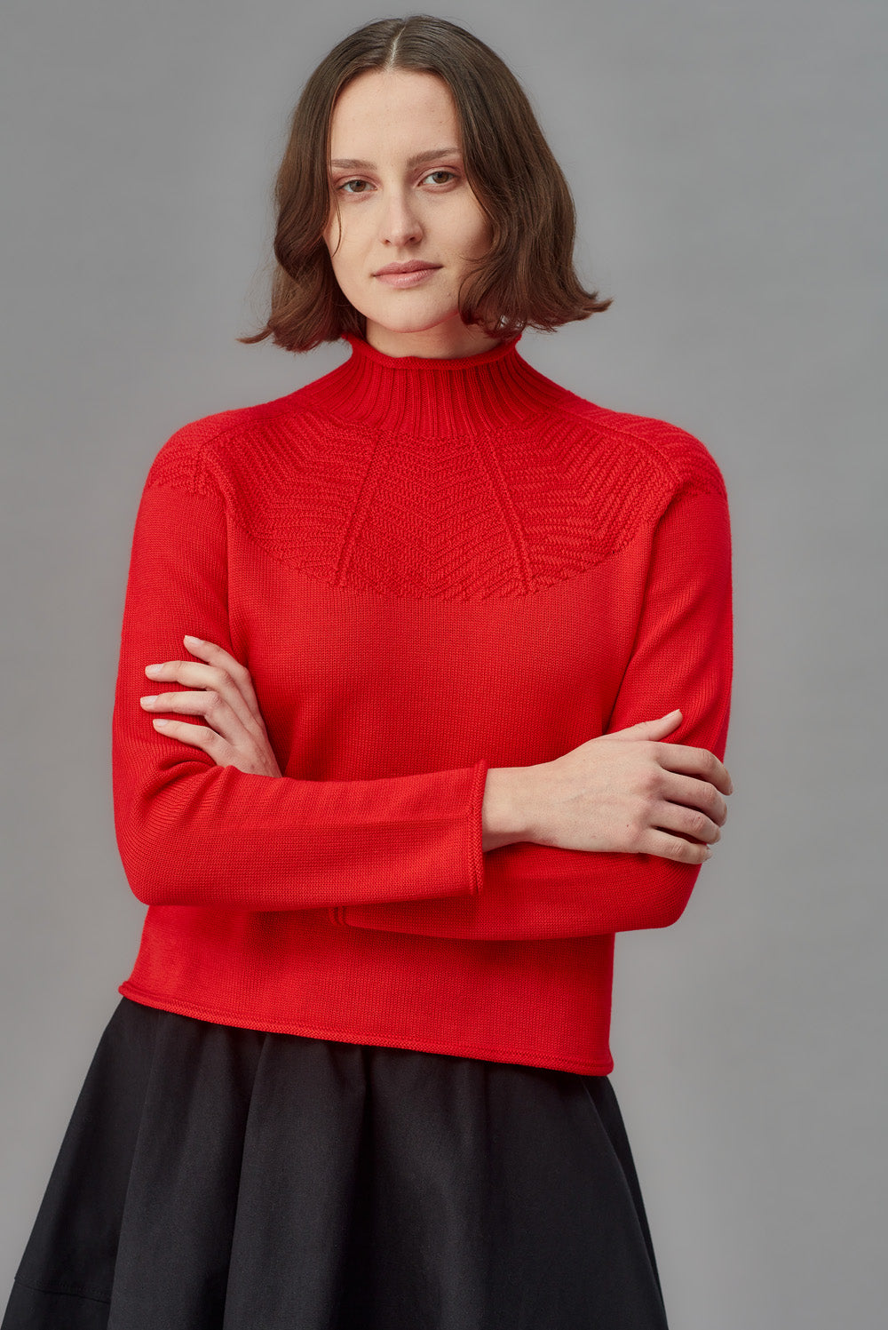 Person wearing a red mock neck sweater against a gray background