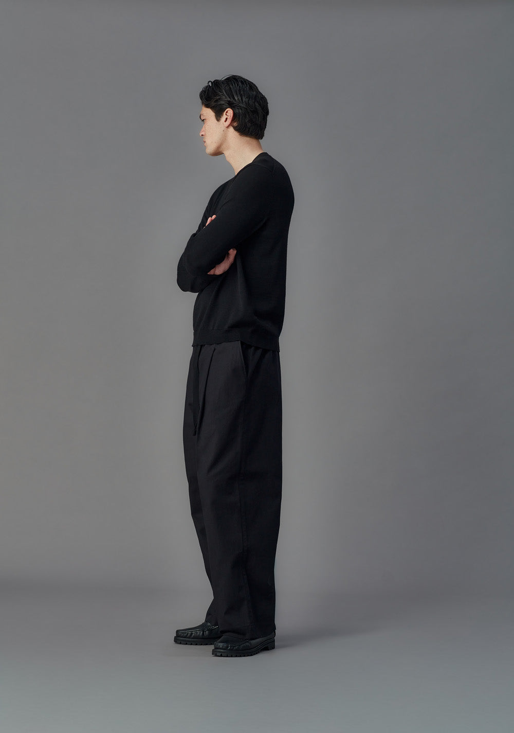 Person wearing a black outfit standing against a gray background