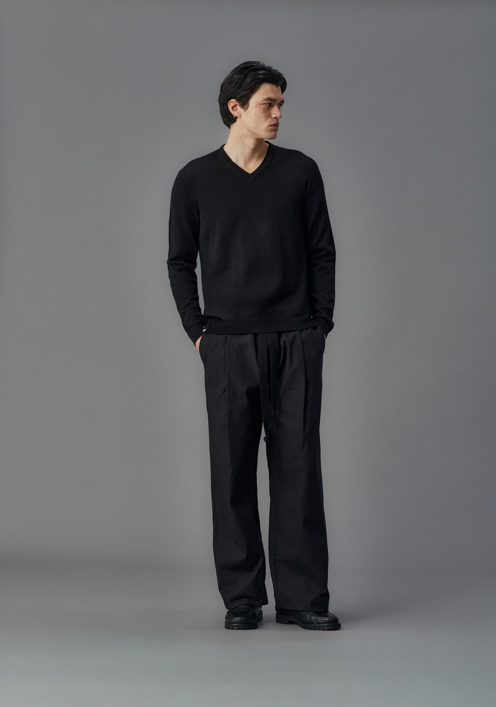 Man wearing a black outfit standing against a gray background