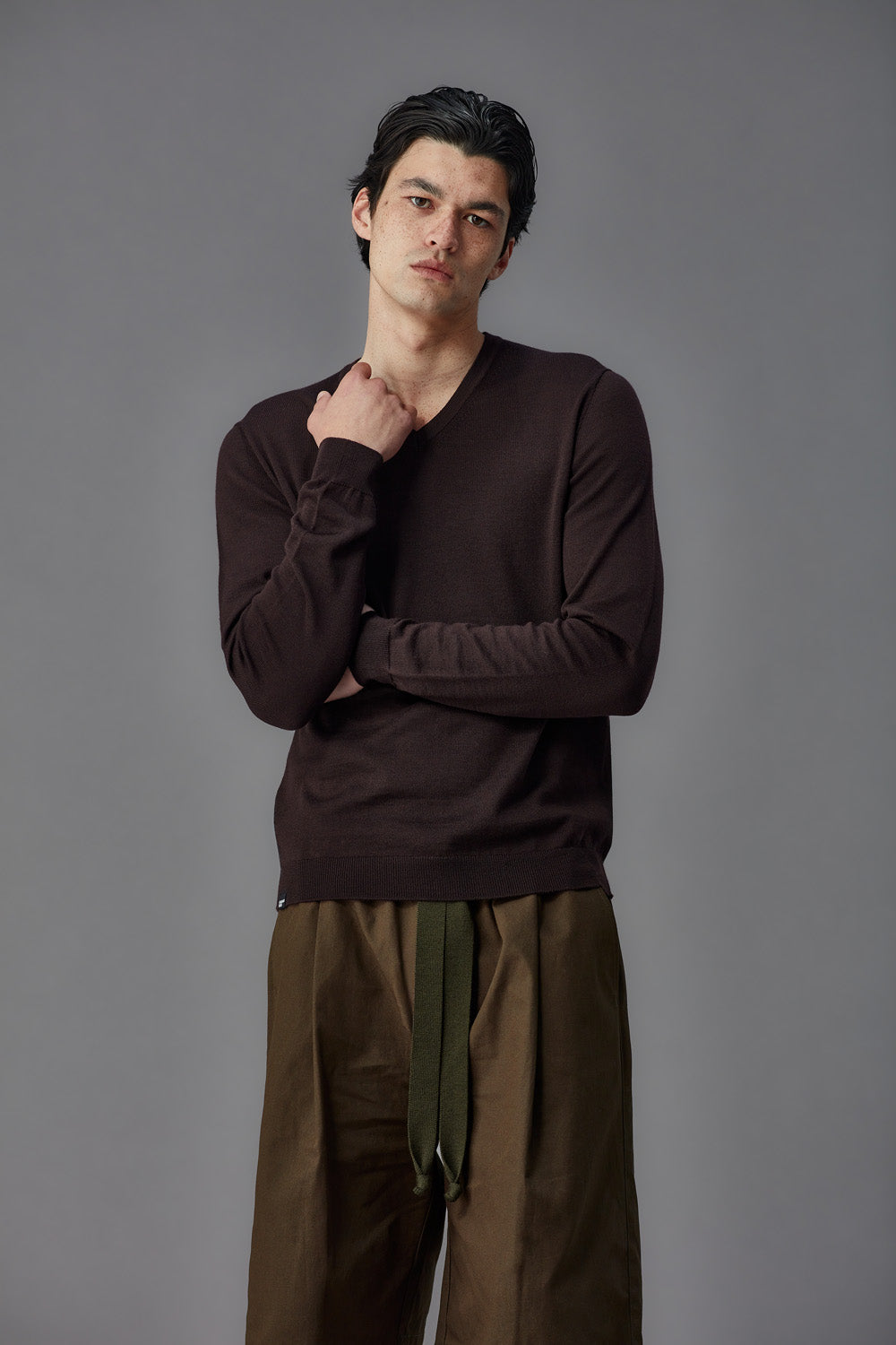 Man wearing a brown long-sleeve shirt and brown pants against a gray background