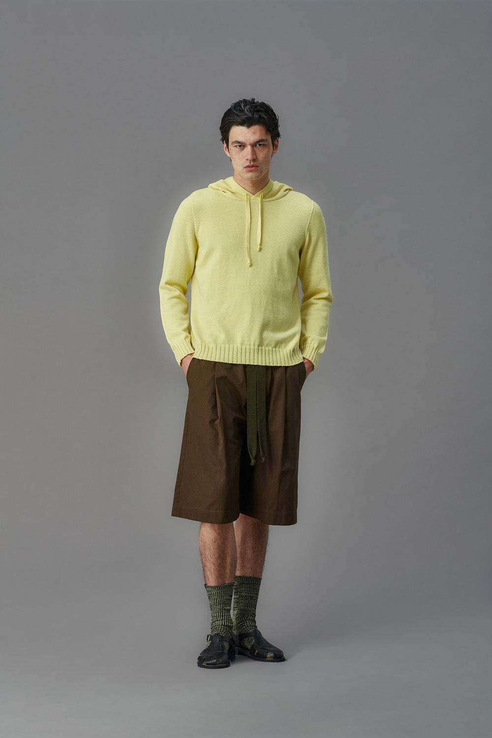 Man wearing a light yellow hoodie and brown shorts on a gray background