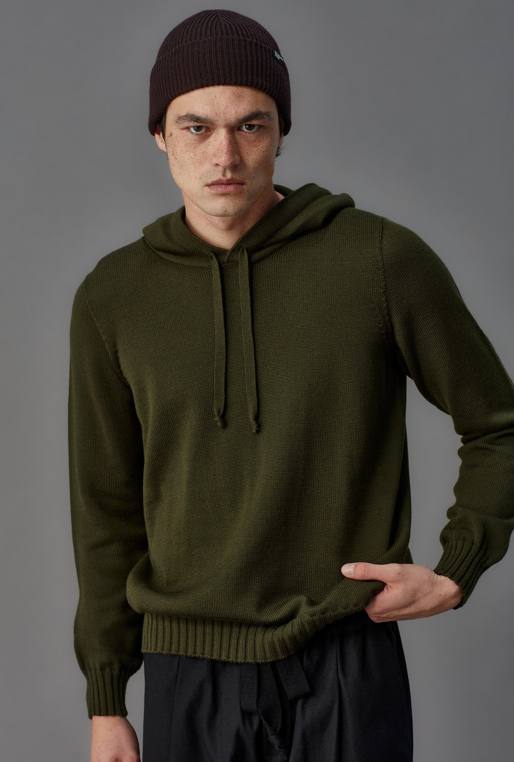 Man wearing a green hoodie and dark beanie against a gray background