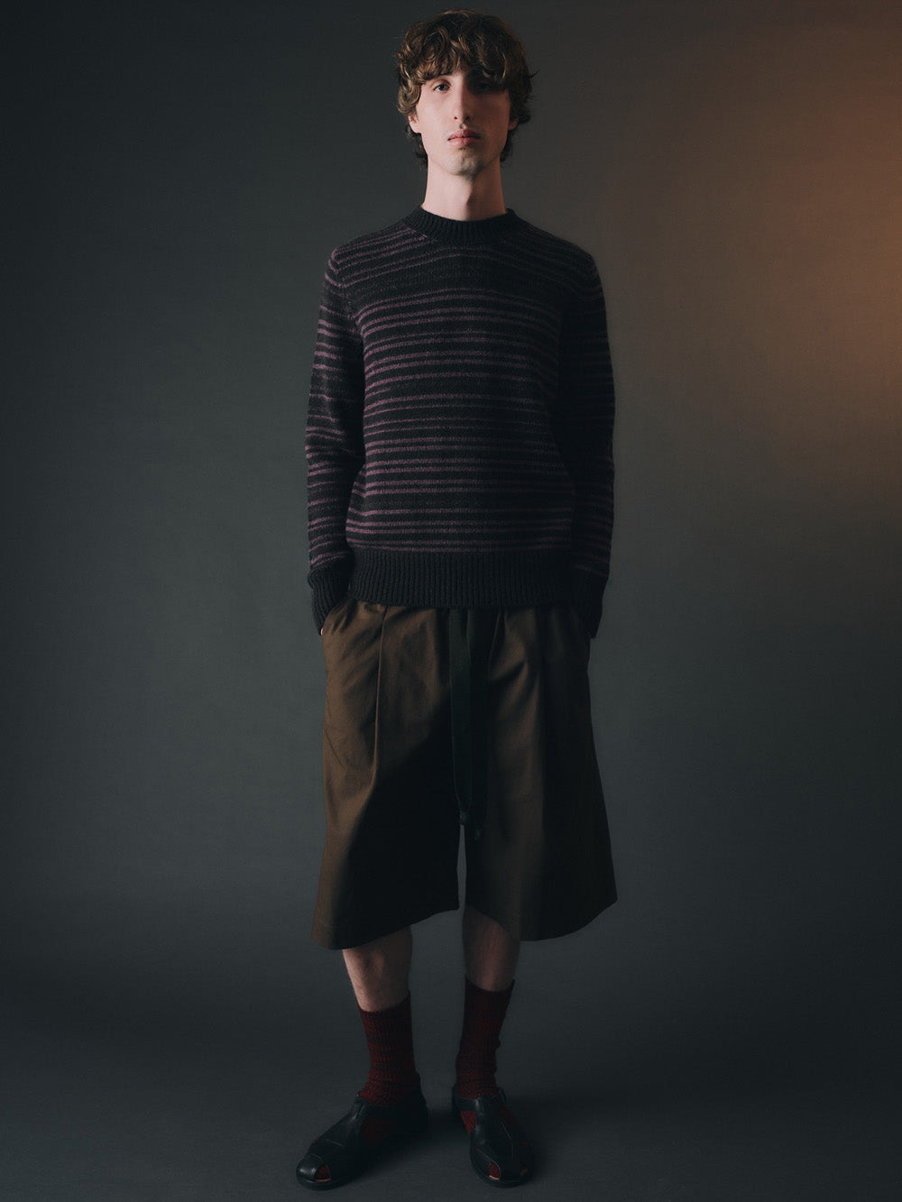 Man wearing a striped sweater and dark pants against a plain background