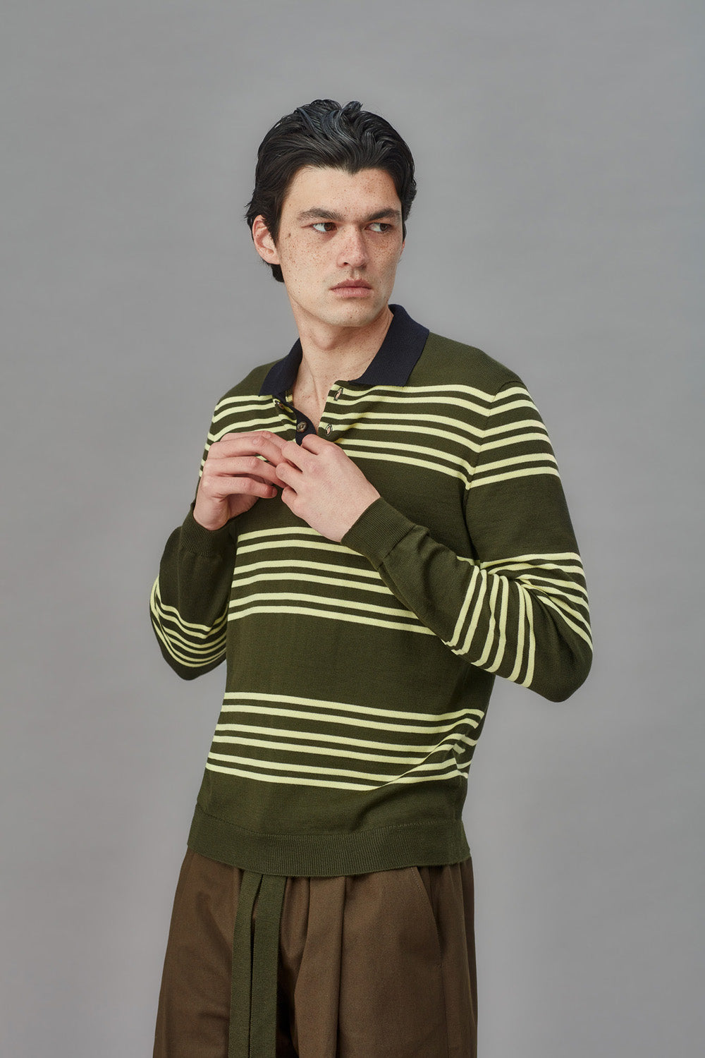 Man wearing a green and yellow striped polo sweater against a gray background