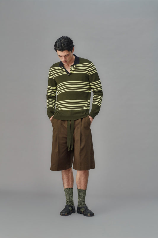 Man wearing a green striped sweater and brown shorts on a gray background