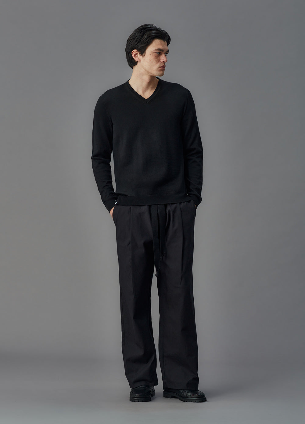 Man wearing a black sweater and pants against a gray background