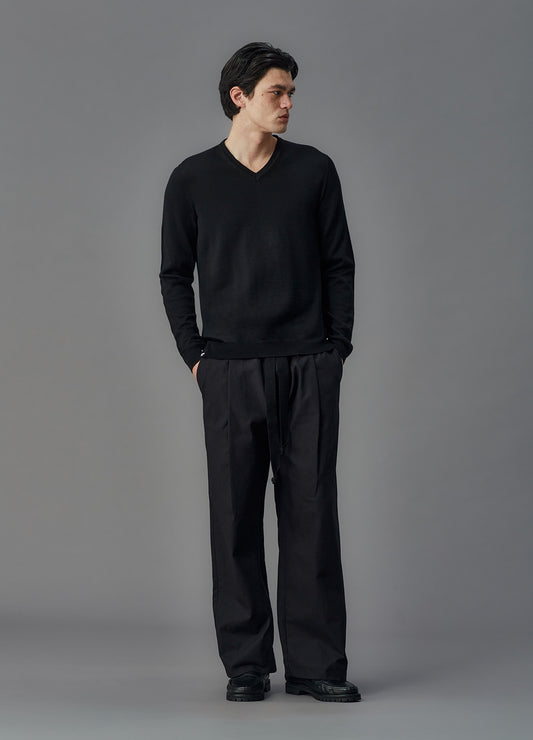 Man wearing a black sweater and pants against a gray background