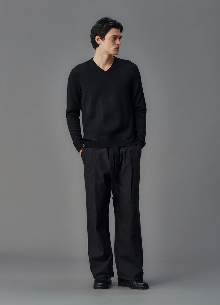 Man wearing a black sweater and pants against a gray background