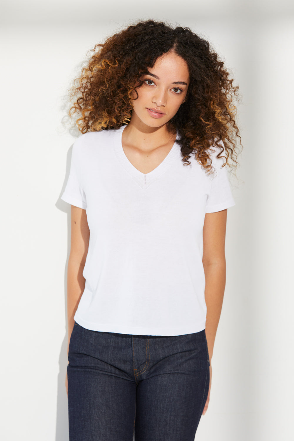 A woman standing wearing a white Standard Issue Cotton Little V Tee.